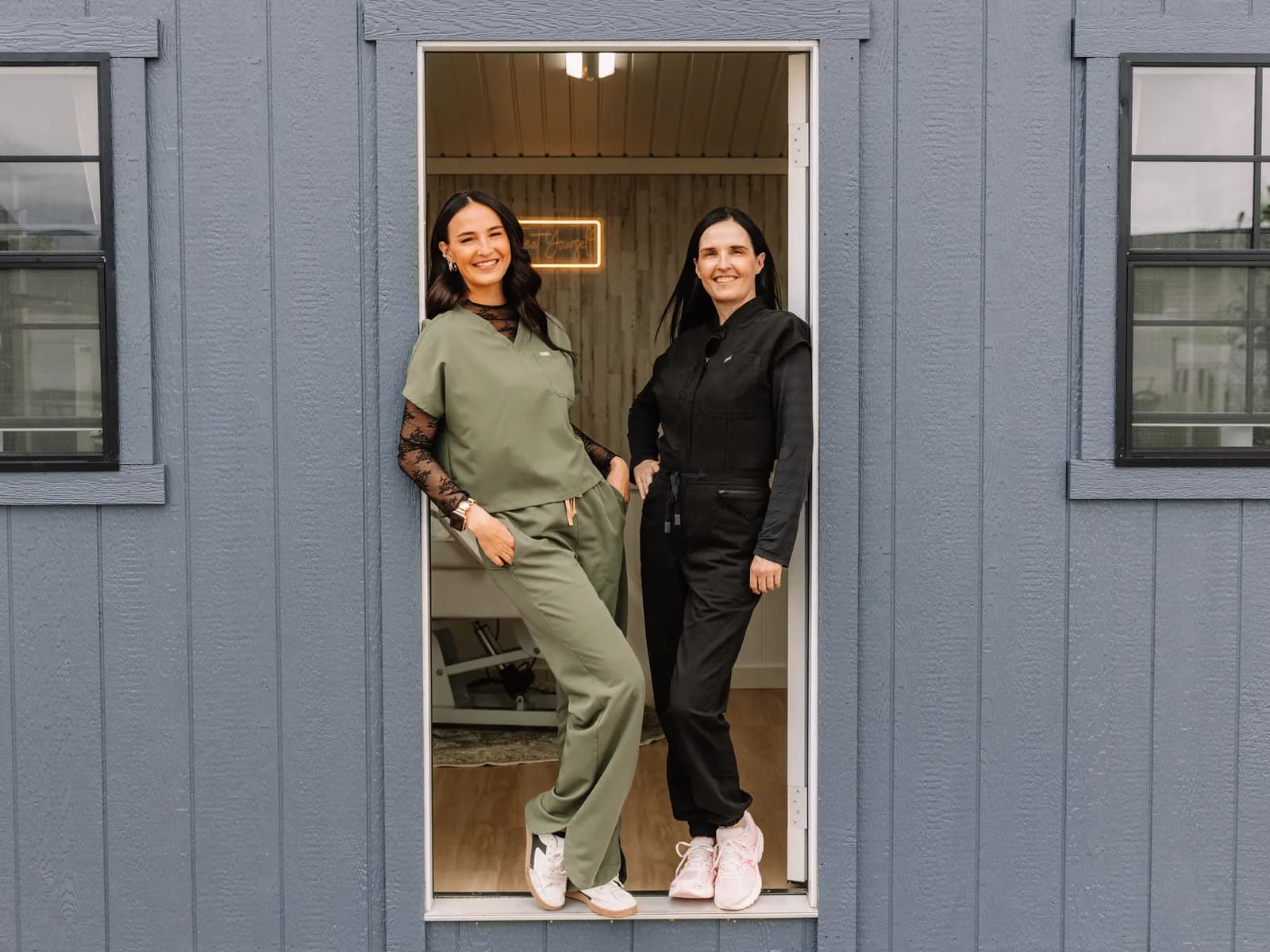 The blue-gray Jaed Aesthetics studio building — Jaedee and Melissa in the doorway