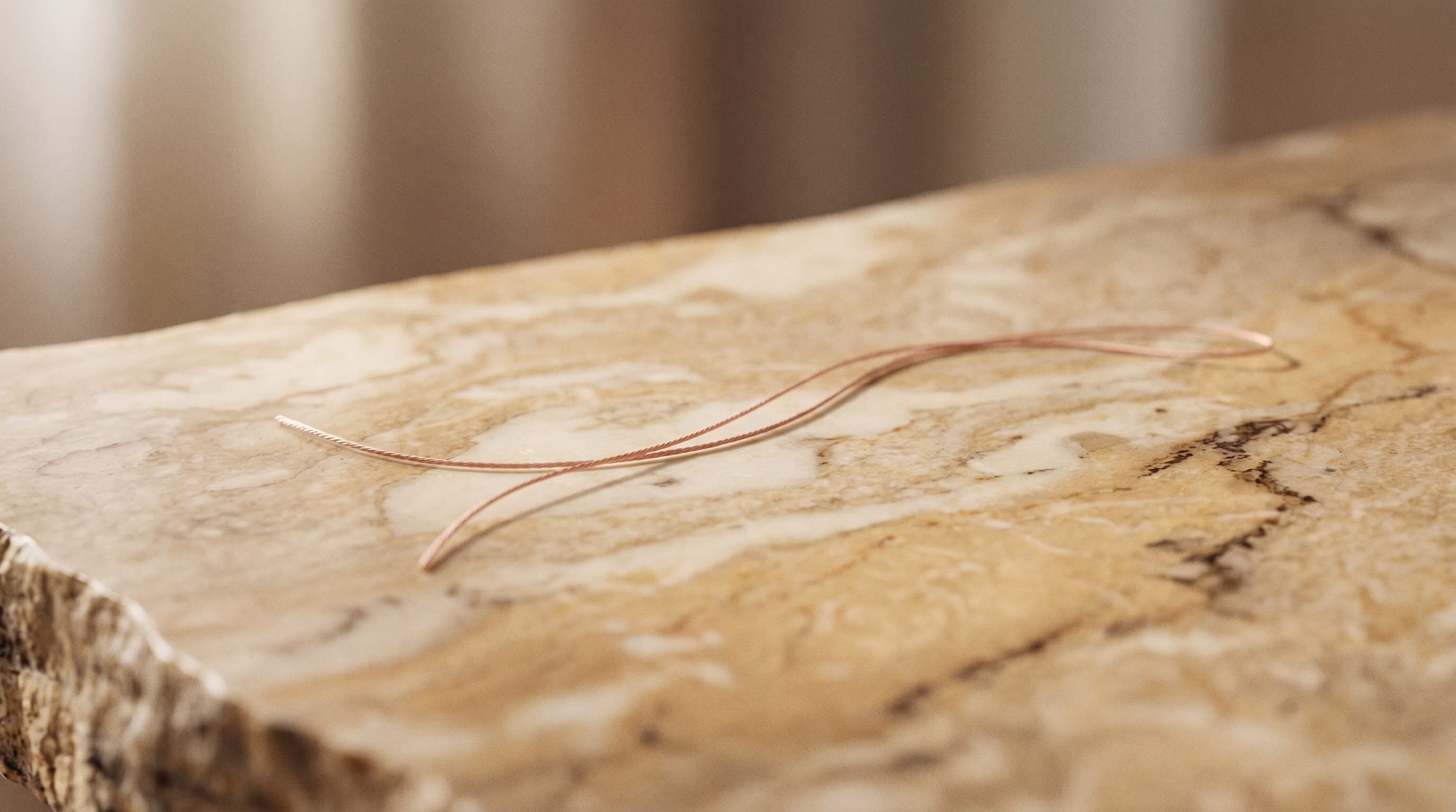 A single rose-gold thread laid across warm marble